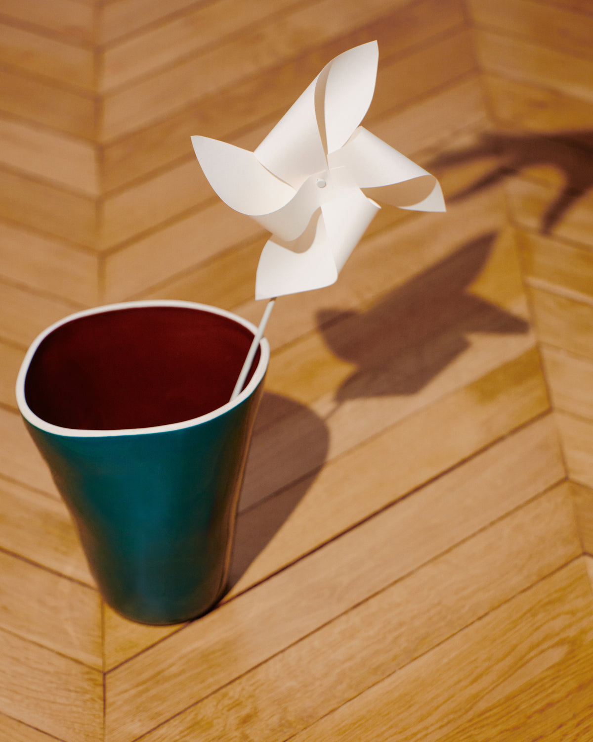 Vase Double Jeu Bleu Sarah/Chocolat et moulin à vent en papier posés sur un parquet en chevrons