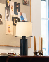 Lampe Portofino Bleu Noir, bougeoir en laiton et bougies fines devant un moodboard en liège