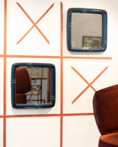 Miroirs Coco Bleu Noir accrochés en morpion sur un mur aux croix terracotta, pouf bordeaux