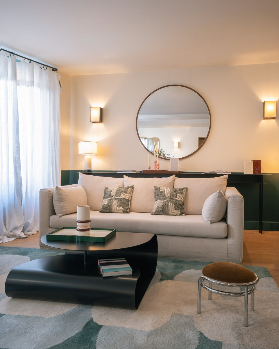 Salon : canapé écru, Miroir Bulle Noyer, table basse noire aux lignes courbes et tabouret chromé